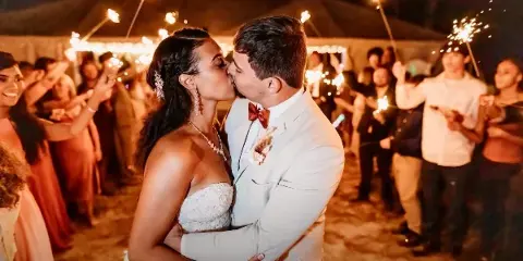 A bride and groom sharing a kiss during a sparkler send-off under a large tent at a rustic wedding venue.