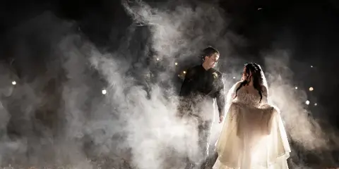 A bride and groom walking through a cloud of white smoke at night.