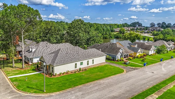 Aerial view of a suburban residential neighborhood featuring single-family homes, manicured lawns, and a pond in the background.