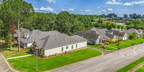Aerial view of a suburban residential neighborhood featuring single-family homes, manicured lawns, and a pond in the background.