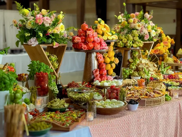 A lavish catering table featuring towering floral arrangements, fruit displays, and an assortment of gourmet dishes.