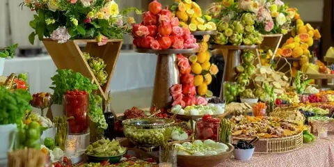 A lavish catering table featuring towering floral arrangements, fruit displays, and an assortment of gourmet dishes.