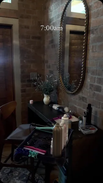 A professional hair and makeup station set up in a brick-walled room, featuring a large mirror, styling tools, and beauty products.