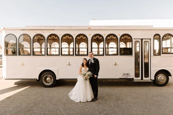 A bride and groom standing in front of a white Michigan Trolley vehicle.