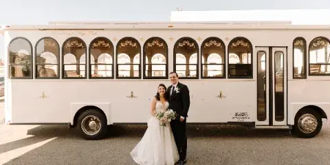 A bride and groom standing in front of a white Michigan Trolley vehicle.