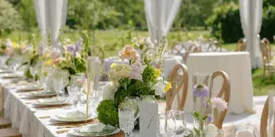 A long wedding reception table set with white linens, green plates, and floral centerpieces inside a white tent.