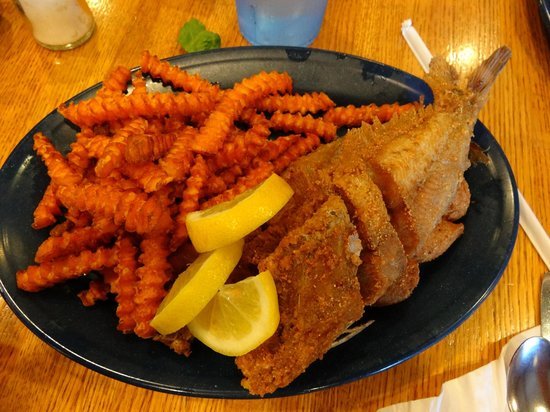 A plate of fried fish and crinkle-cut fries with lemon wedges on a wooden table.