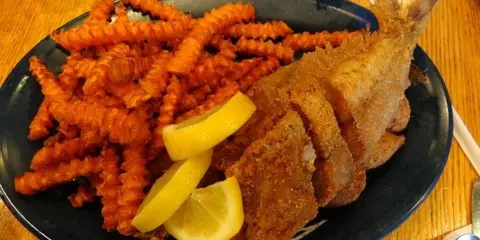 A plate of fried fish and crinkle-cut fries with lemon wedges on a wooden table.