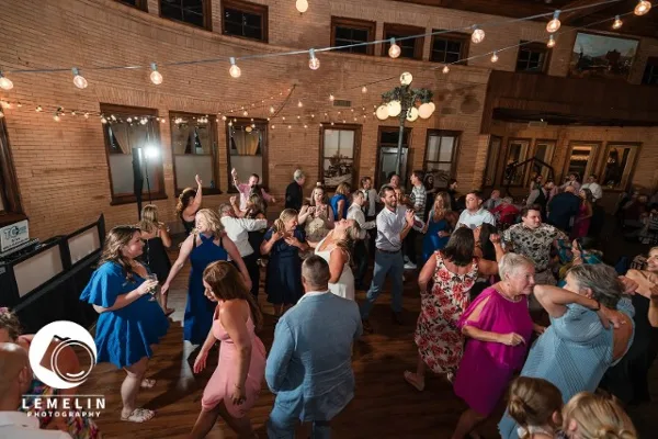 Guests dancing at a wedding reception in a venue with string lights and brick walls.