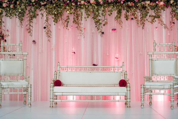 Wedding lounge setup with pink draping, floral garland, and white upholstered seating.