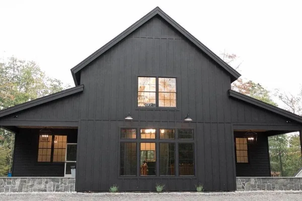 Exterior view of a modern black barn wedding venue with large windows and stone foundation.