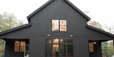 Exterior view of a modern black barn wedding venue with large windows and stone foundation.