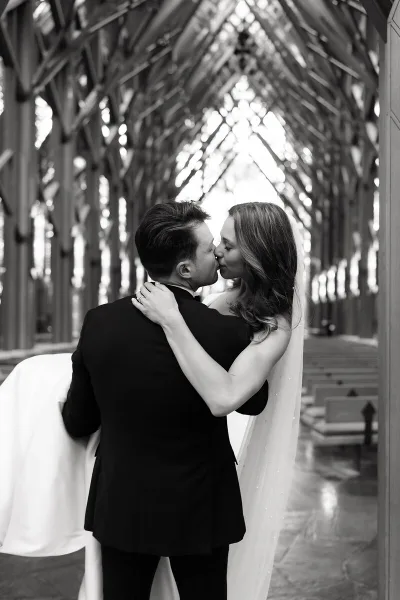 A black and white photograph of a bride and groom kissing inside a church with high vaulted ceilings.