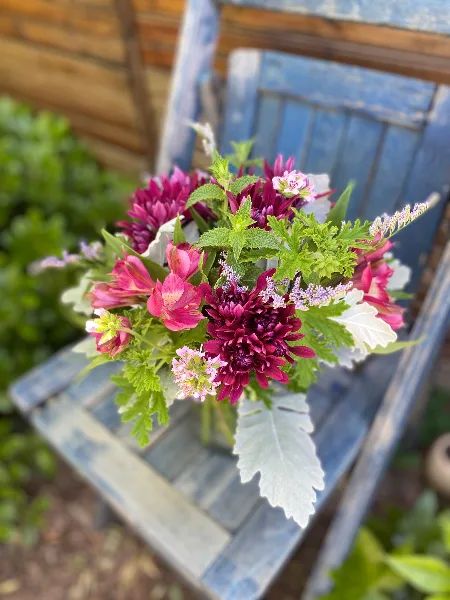 A floral bouquet containing pink alstroemeria and dark red mums arranged on a blue wooden bench.