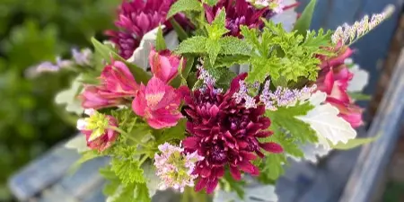 A floral bouquet containing pink alstroemeria and dark red mums arranged on a blue wooden bench.