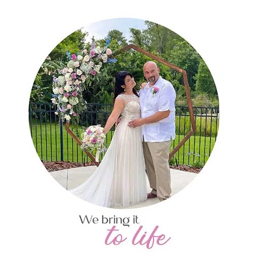 A bride and groom posing in front of a floral wedding archway with a bouquet.