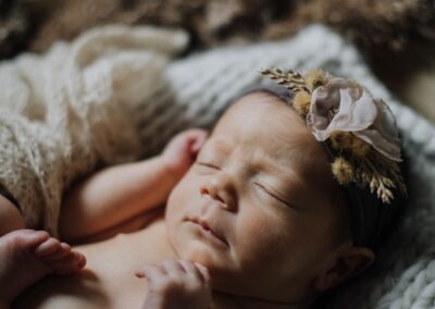 A sleeping newborn baby wearing a floral headband, resting on a textured blanket.