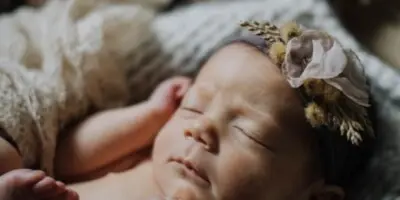 A sleeping newborn baby wearing a floral headband, resting on a textured blanket.