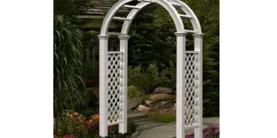 A white decorative garden archway standing in a landscaped outdoor setting.