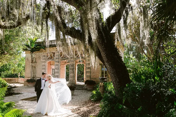 A bride and groom standing together in a garden with Spanish moss hanging from a large tree.