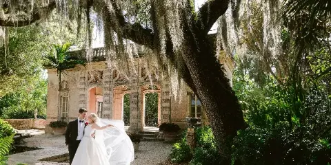 A bride and groom standing together in a garden with Spanish moss hanging from a large tree.