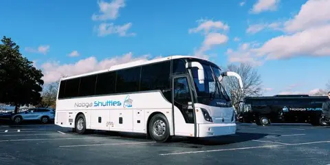 A white Nooga Shuttles charter bus parked in a lot under a blue sky.