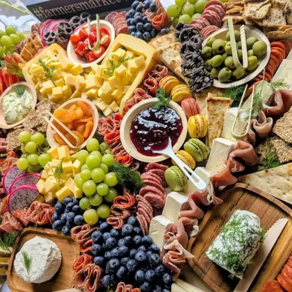 A close-up view of a catering grazing table featuring an assortment of cheeses, cured meats, grapes, and blueberries.