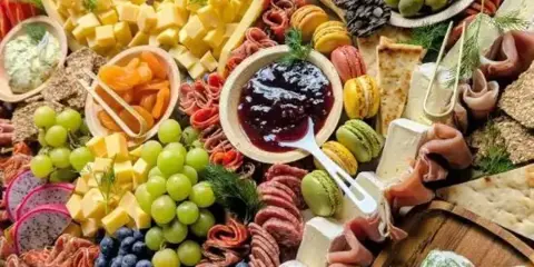 A close-up view of a catering grazing table featuring an assortment of cheeses, cured meats, grapes, and blueberries.
