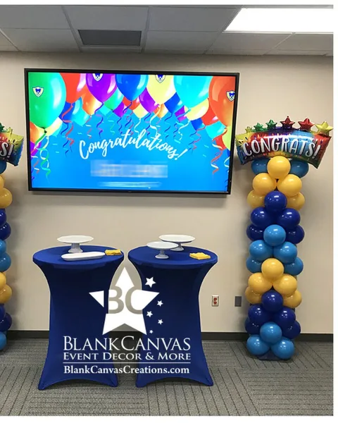 A corporate event space decorated with blue and yellow balloon columns, a 'Congratulations' balloon, and a table with a Blank Canvas Event Decor skirt.