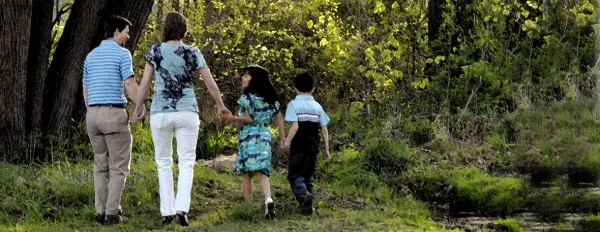 A family of four walking hand-in-hand along a wooded path.