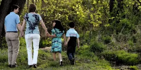 A family of four walking hand-in-hand along a wooded path.