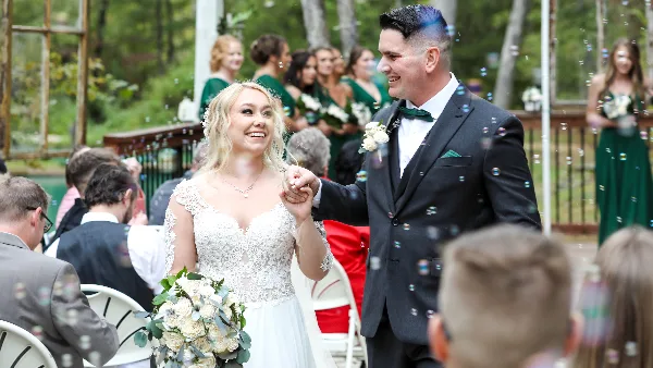 A bride and groom walking down the aisle during a wedding ceremony with bubbles in the air.