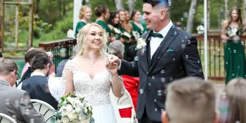 A bride and groom walking down the aisle during a wedding ceremony with bubbles in the air.