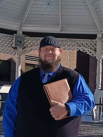 Dennis Richardson, a wedding officiant, standing in front of a white gazebo holding a book.