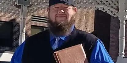 Dennis Richardson, a wedding officiant, standing in front of a white gazebo holding a book.