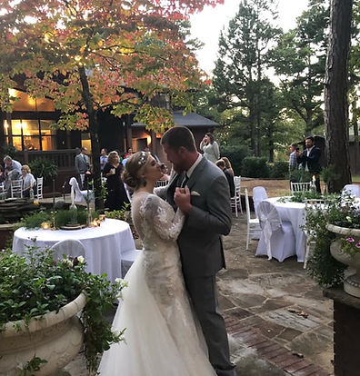 A bride and groom dancing at an outdoor wedding reception with set tables and a natural background.