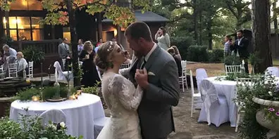 A bride and groom dancing at an outdoor wedding reception with set tables and a natural background.