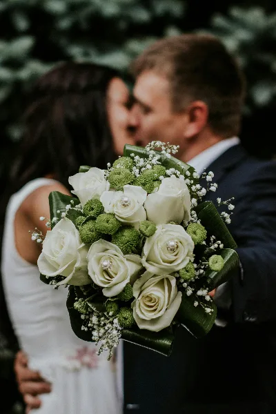 Wedding couple kissing with a white rose and greenery bouquet in the foreground
