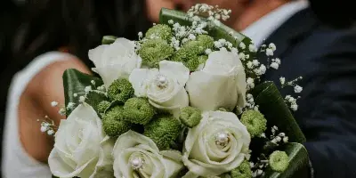 Wedding couple kissing with a white rose and greenery bouquet in the foreground