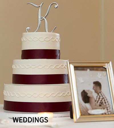 A three-tiered white and maroon wedding cake with a silver monogram topper.