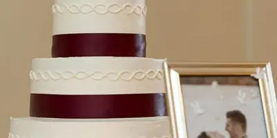 A three-tiered white and maroon wedding cake with a silver monogram topper.