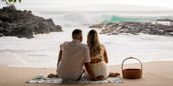 A couple sitting on a beach looking out at the ocean waves.