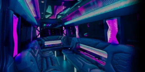 Interior view of a luxury party bus with blue and purple ambient lighting and plush leather seating.