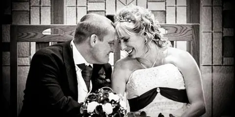 A black and white photograph of a bride and groom smiling at each other during a wedding ceremony.