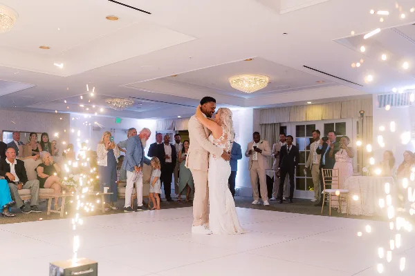 A couple shares their first dance at a wedding reception while guests watch and cold sparklers light up the room.