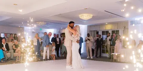 A couple shares their first dance at a wedding reception while guests watch and cold sparklers light up the room.