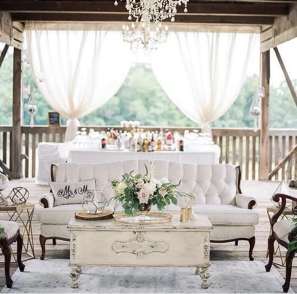A wedding lounge setup with a white sofa, coffee table, and floral centerpiece in a rustic venue.