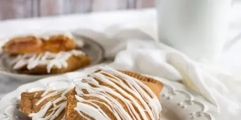 Two golden-brown fried pies drizzled with white icing on a white plate, with a cup of coffee in the background.