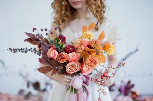 A bride holding a large, intricate floral bouquet featuring roses, dahlias, and dried botanicals.