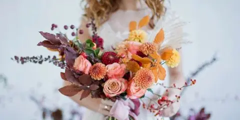 A bride holding a large, intricate floral bouquet featuring roses, dahlias, and dried botanicals.